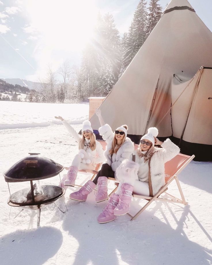 Women in fur coats sitting in the snow by a fire pit